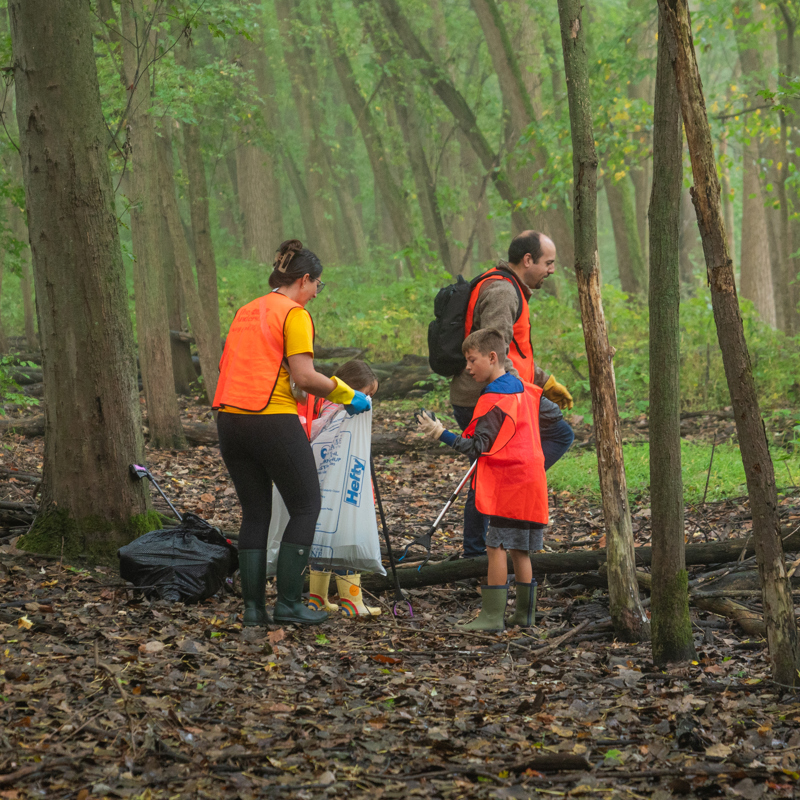 Employees and children cleaning up trash in woods