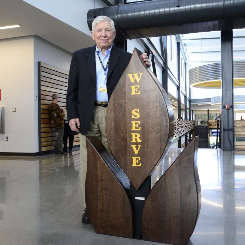 Dick Anderson standing in The Andersons headquarters entry with "We Serve" statue