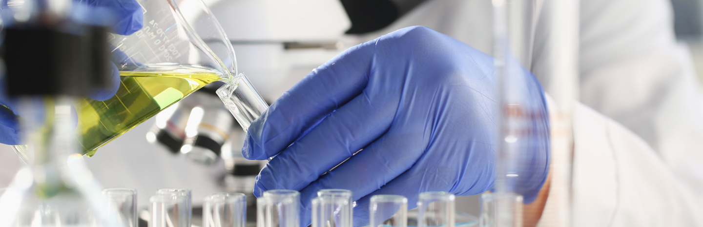 Individual performing test in lab, pouring liquid from a beaker into a test tube while wearing gloves